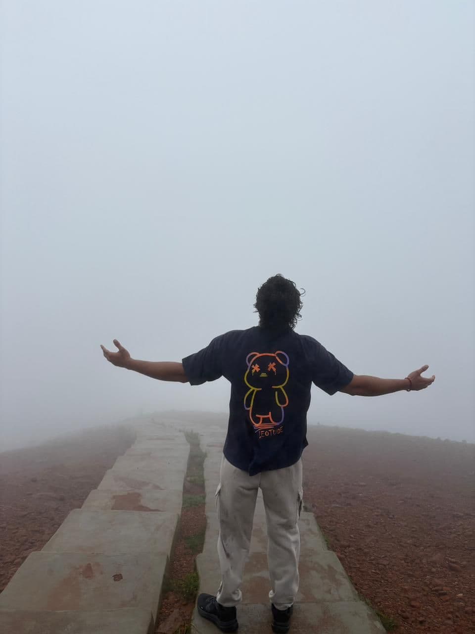 A traveller with arms open on a fog-covered summit